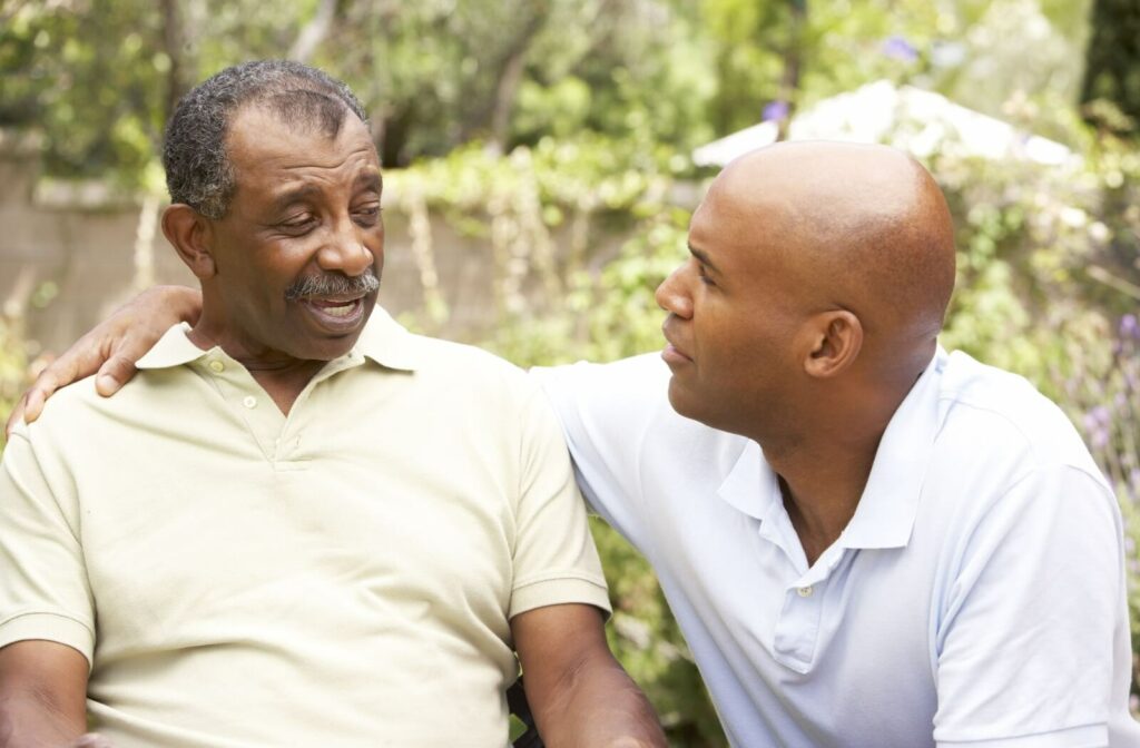 A younger adult gently comforts an older adult during a conversation outdoors, placing a reassuring hand on their shoulder