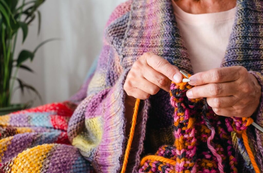 Senior knitting a colorful blanket, wrapped in a cozy handmade shawl.