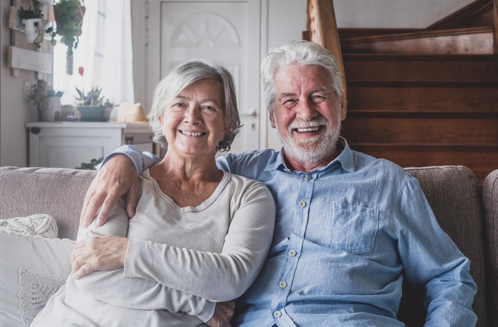 An older couple sitting together on their couch in personal care and smiling.