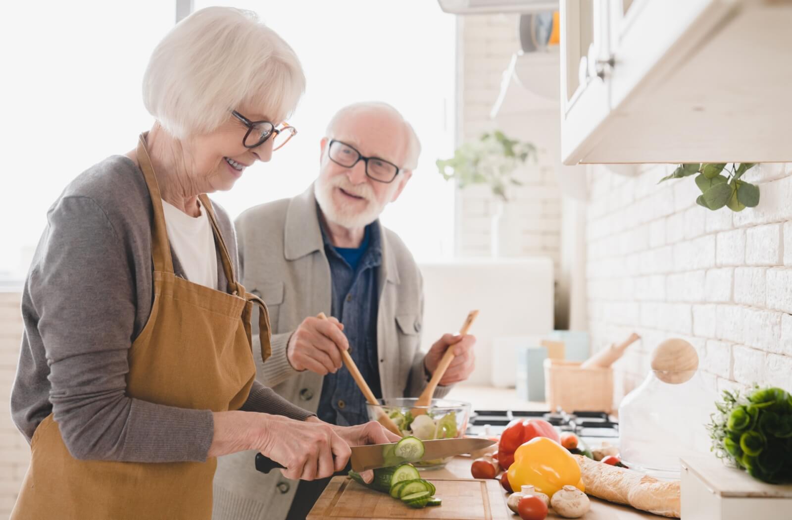 An older adult smiling at their spouse while they prepare an anti-inflammatory salad together.