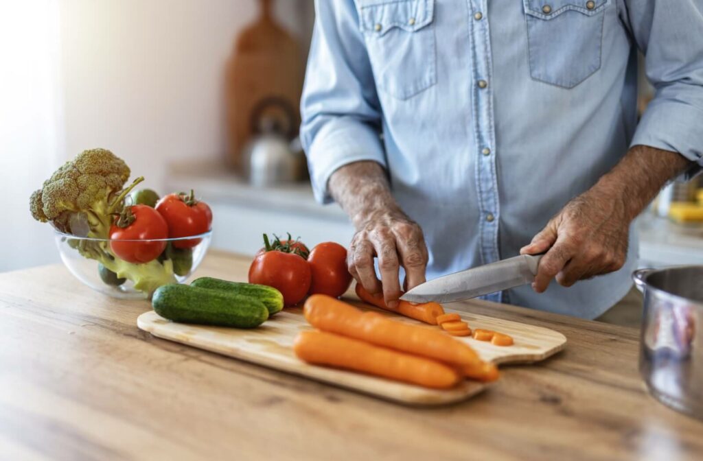 A close-up image of an older adult cutting carrots, cucumbers, and tomatoes for an anti-inflammatory salad.