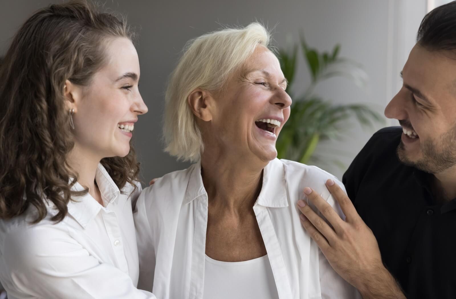 An older adult laughs during a conversation in assisted living with their two adult children