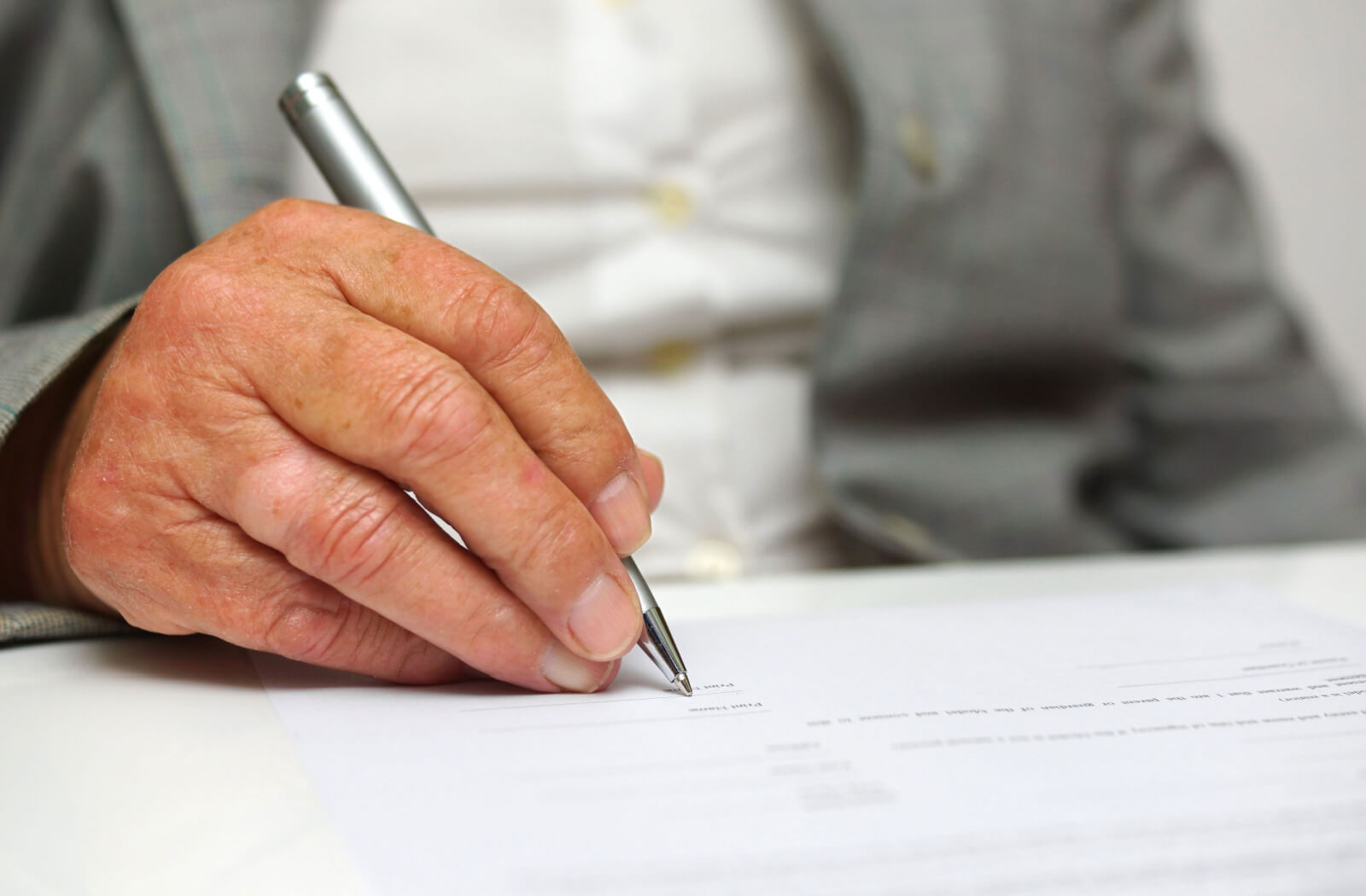 Close-up of an older adult man's right hand, holding a pen and signing a legal paper