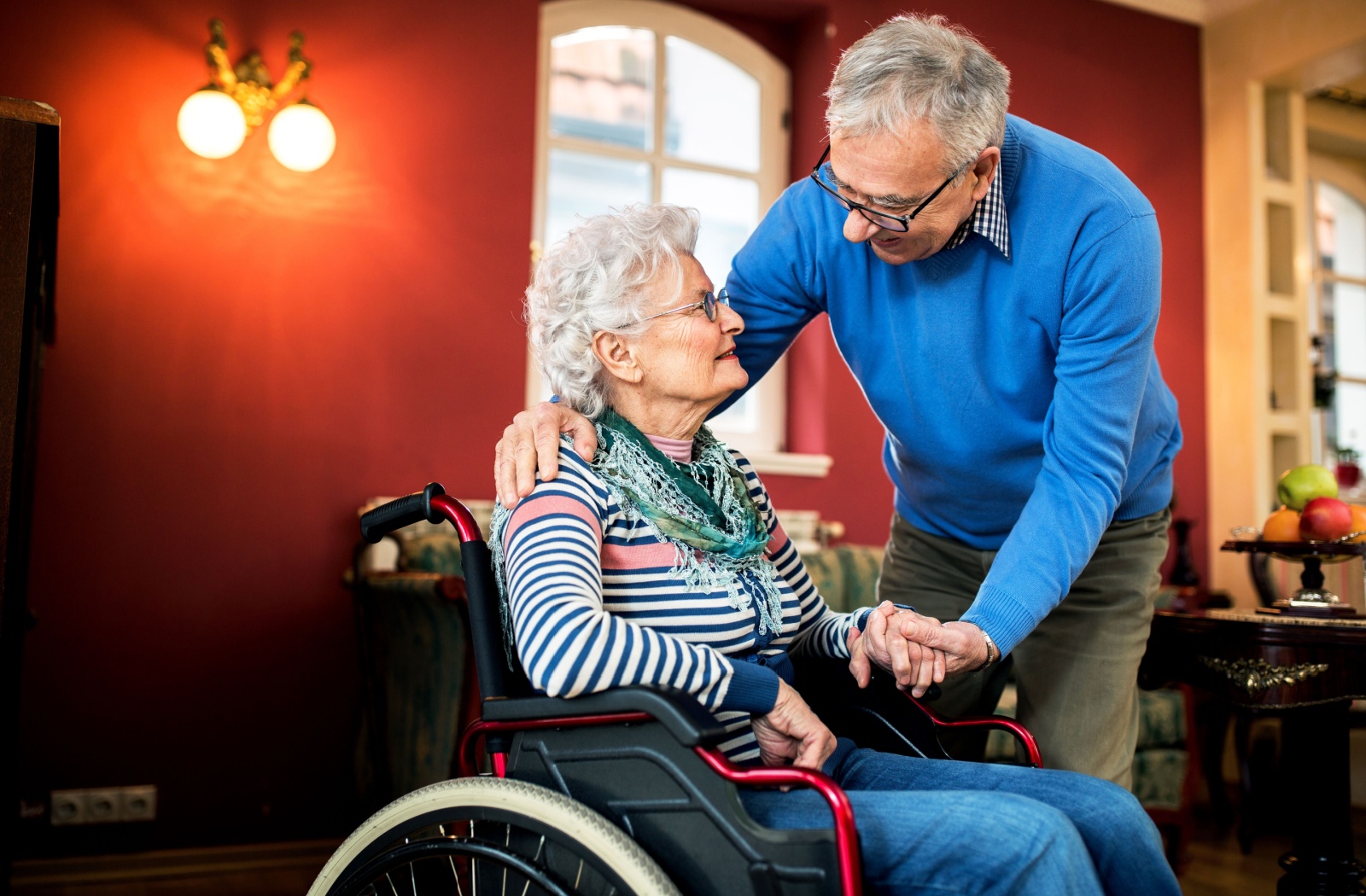 An older adult takes care of their spouse who is in a wheelchair.
